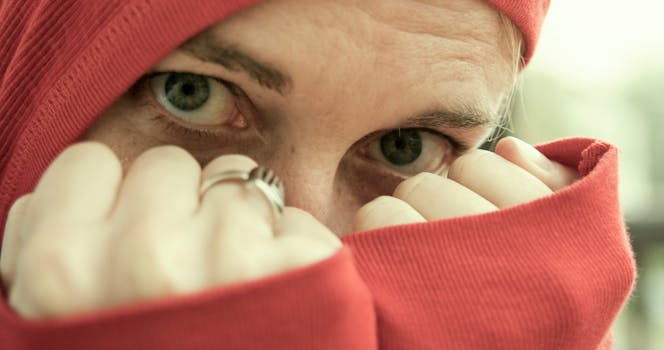 A close-up portrait of a woman with intense eyes and a red hoodie covering her face.
